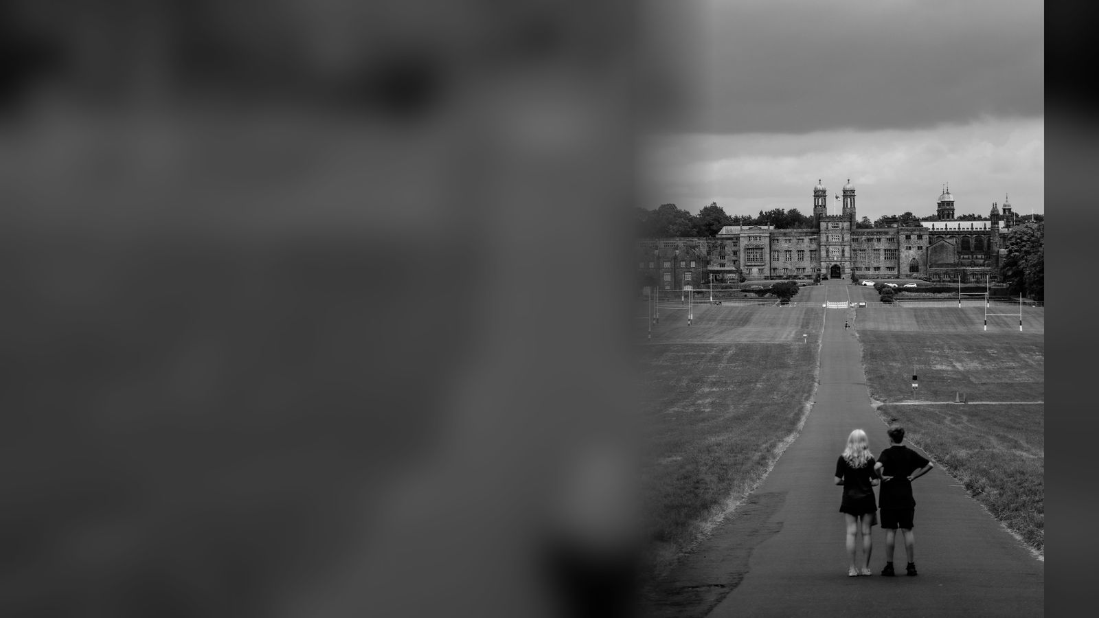 Two students standing on a long path facing a grand college building