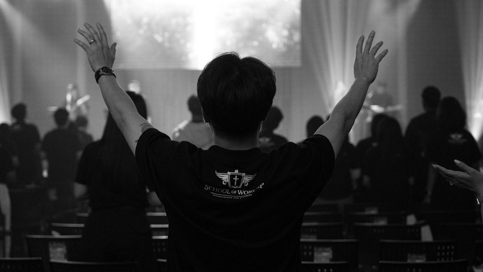A worshipper from behind with both arms raised in a church service