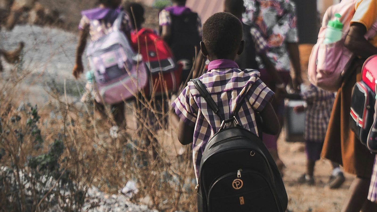 Primary school pupils in uniform with backpacks walking home along a dirt road