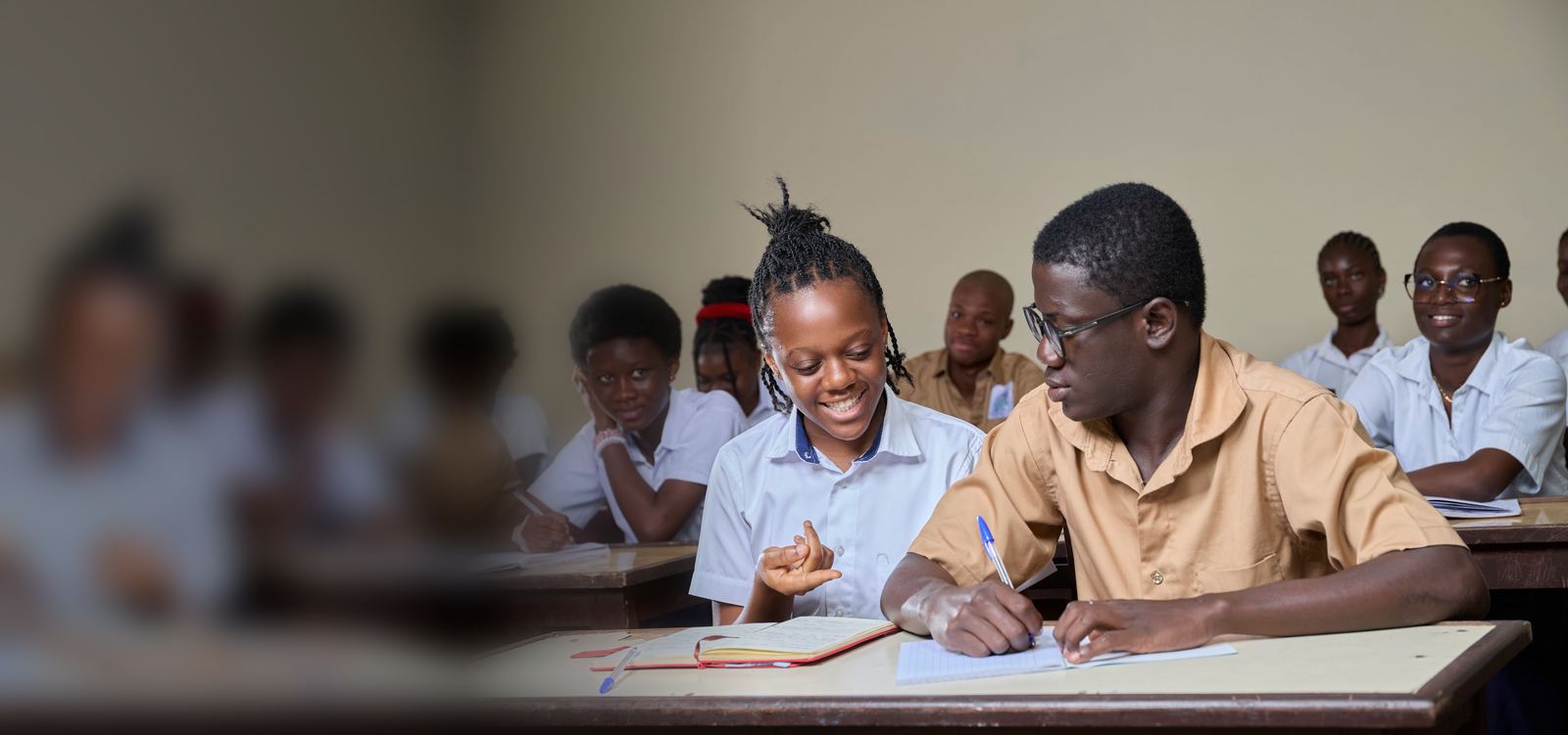 A teenage girl and boy in school uniform smiling and working together in a classroom