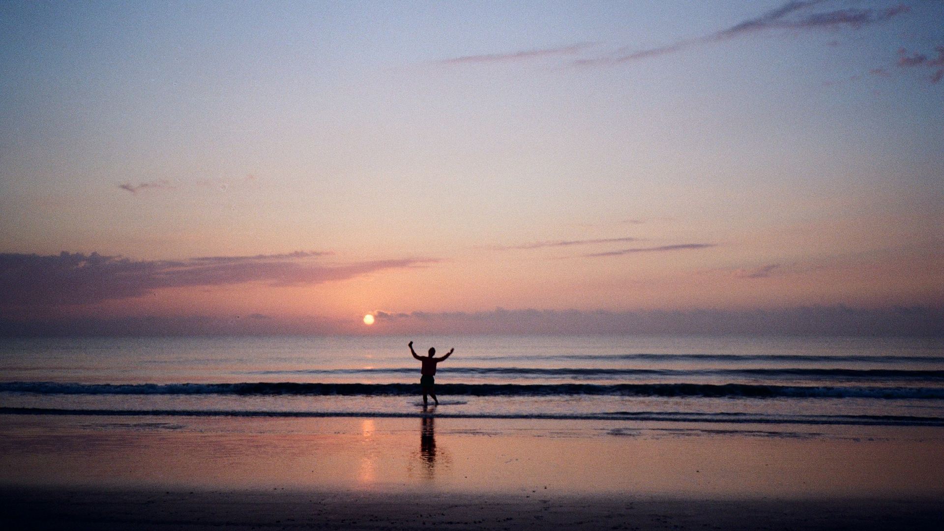A person with arms raised toward the sunrise over the sea, a picture of freedom