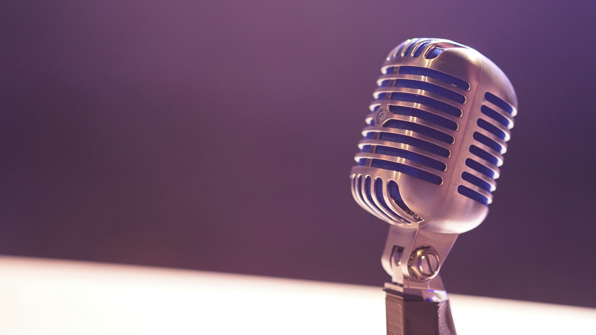 A vintage silver microphone against a soft purple background